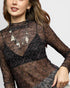 Woman wearing a sheer black long-sleeve top with floral patterns on a plain background