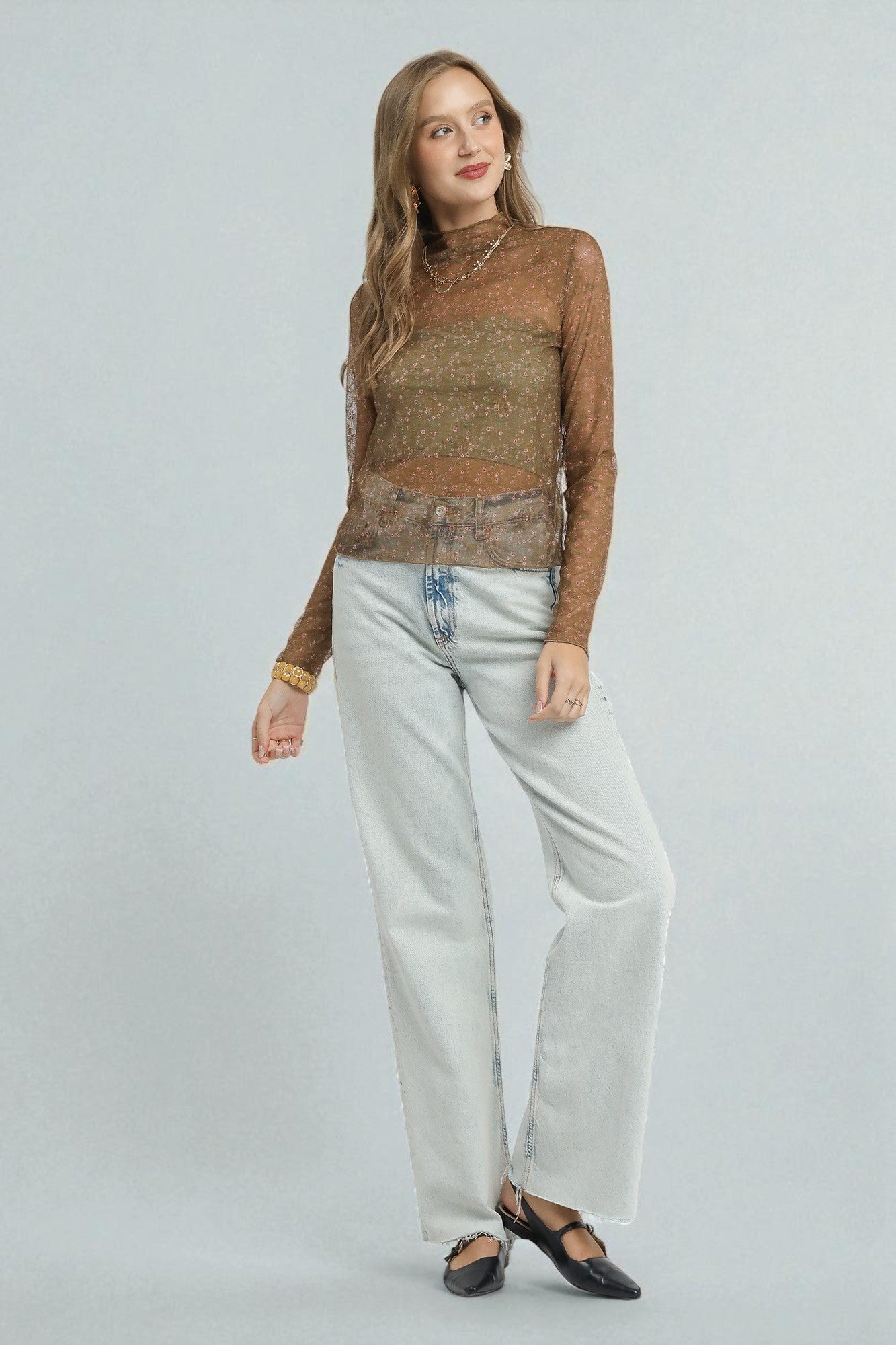 Woman wearing a brown top and light blue jeans on a plain background