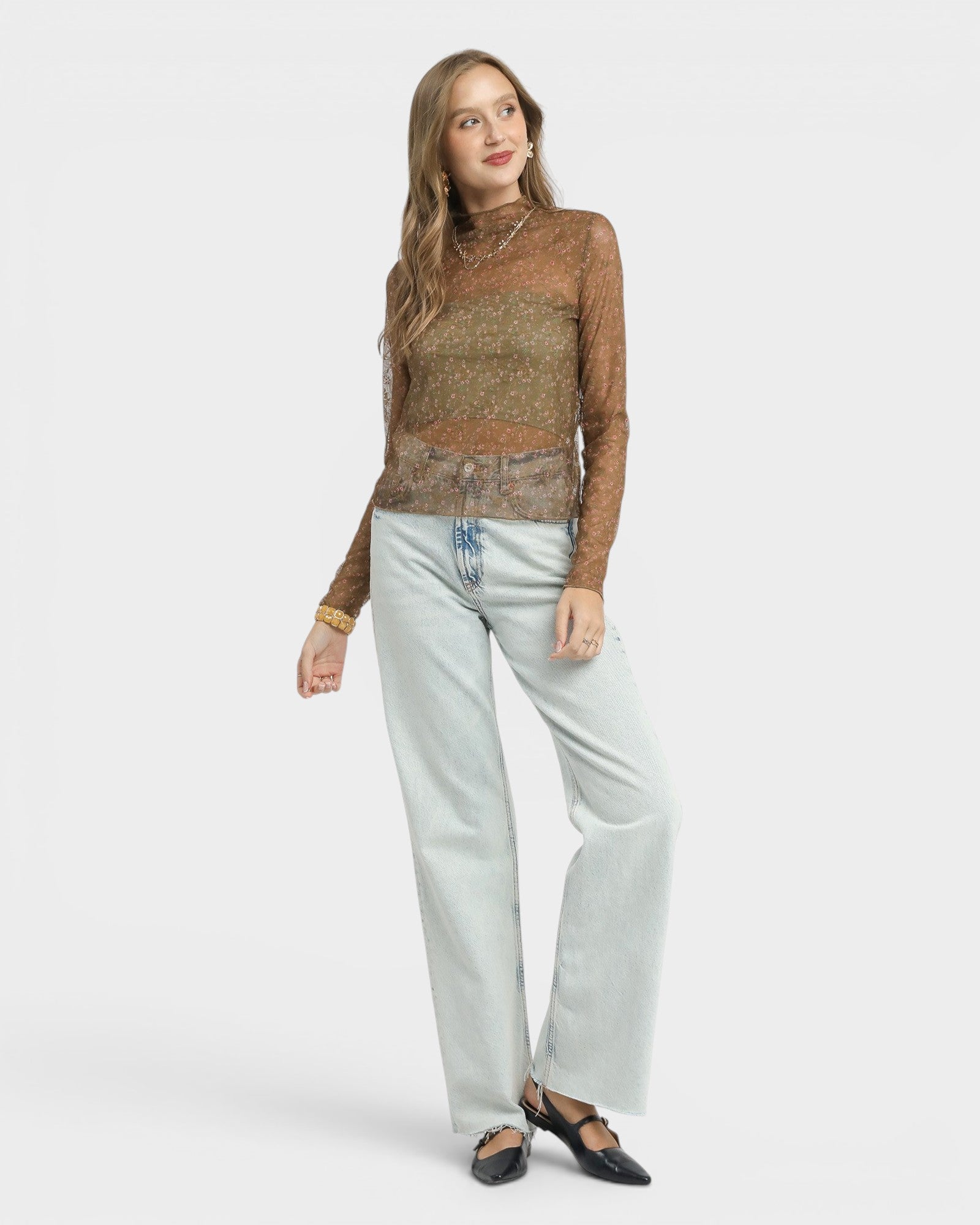 Woman wearing a brown patterned top and light blue jeans on a white background