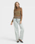 Woman wearing a brown patterned top and light blue jeans on a white background