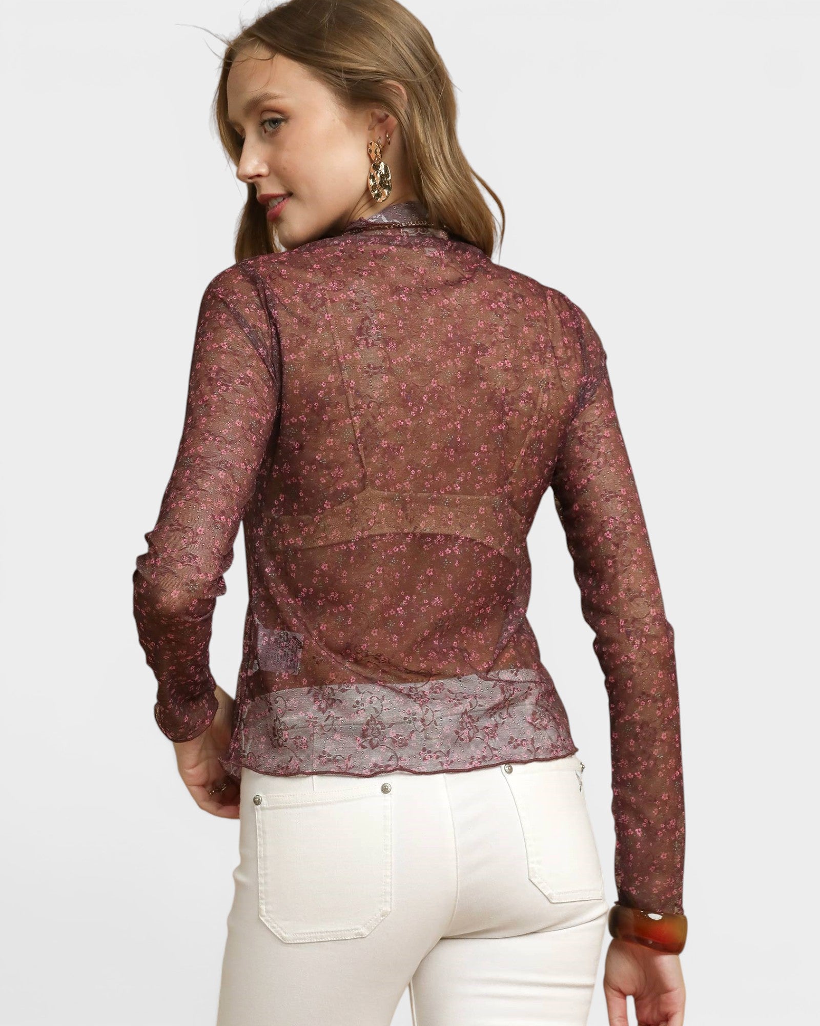 Woman wearing a sheer maroon lace top with white pants on a light gray background