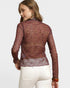 Woman wearing a sheer maroon lace top with white pants on a light gray background