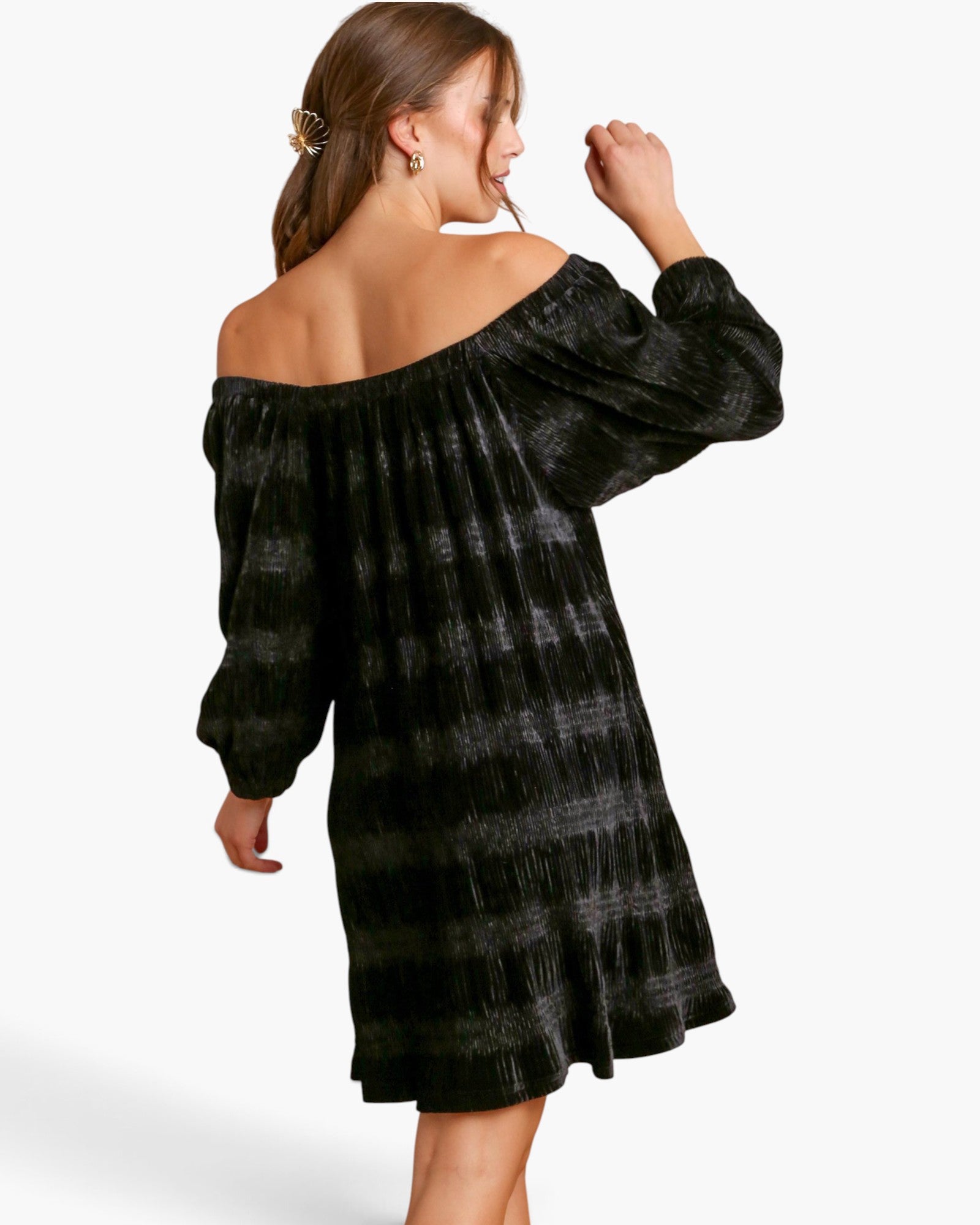 A woman modeling an off-the-shoulder black dress with a textured, crinkled fabric and a subtle horizontal striped pattern, shown from a three-quarters back view against a white studio background.