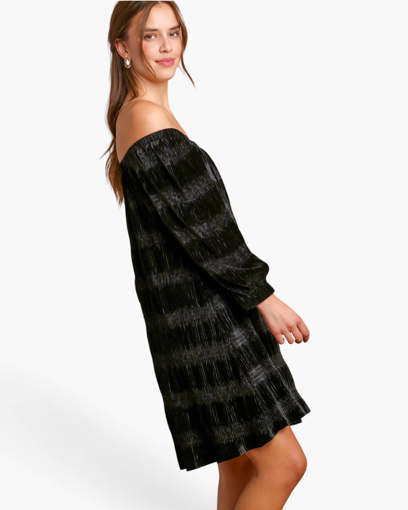 A woman modeling an off-the-shoulder black dress with a textured, shimmering gray plaid pattern, photographed against a clean white studio background.