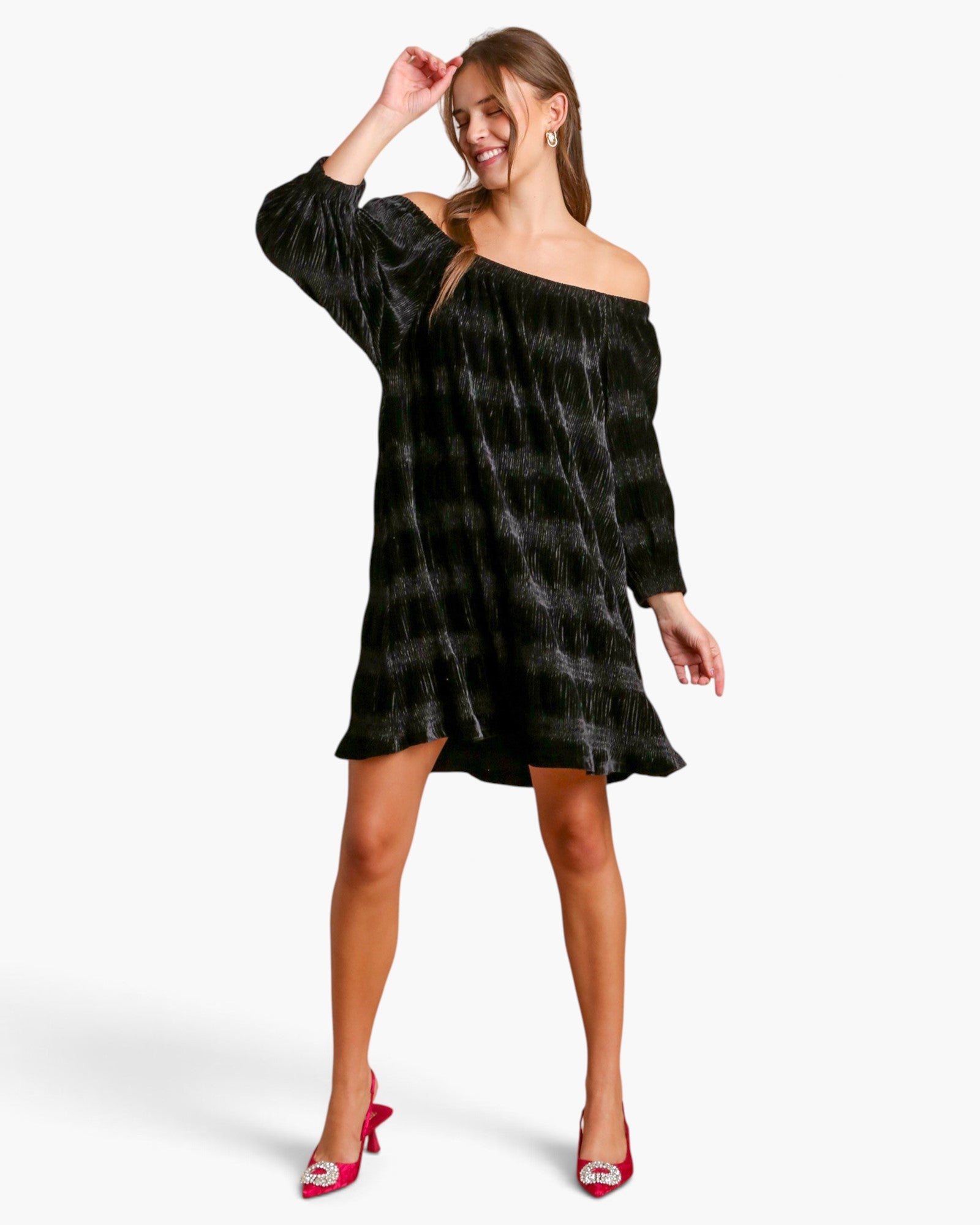 A woman modeling an off-the-shoulder black velvet mini dress with a subtle gray plaid pattern, paired with red high heels, against a plain white studio background.