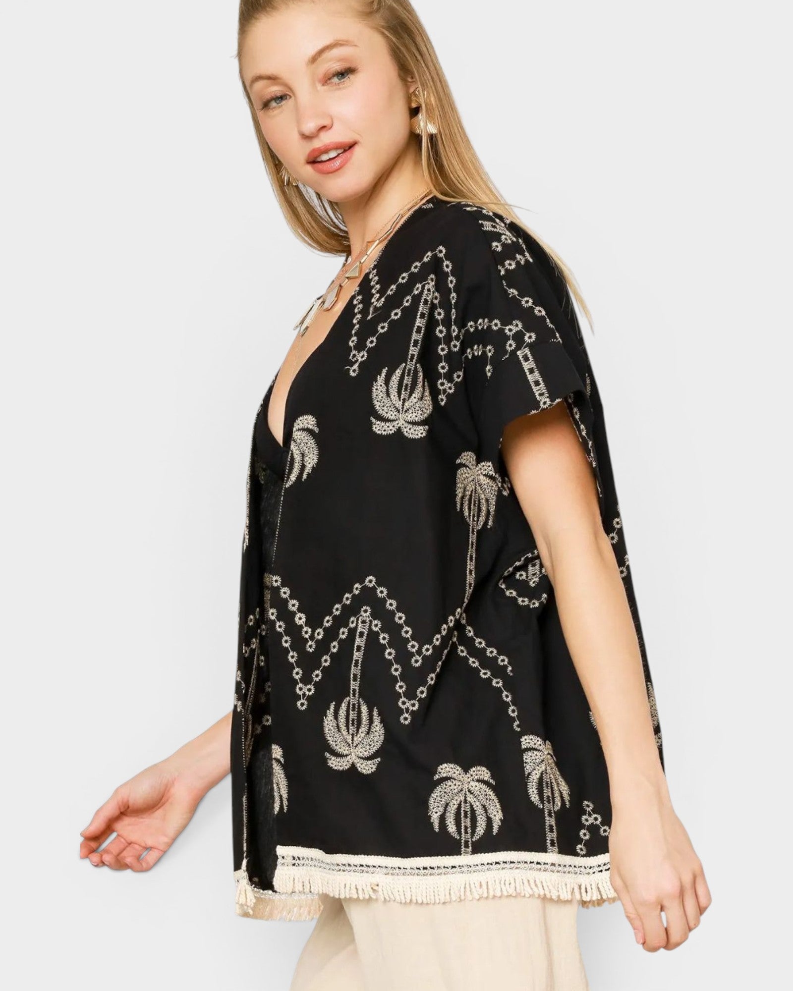 Woman wearing a black embroidered top with palm tree designs on a white background