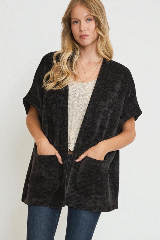 Woman wearing a black velvet poncho over a white top and jeans on a white background
