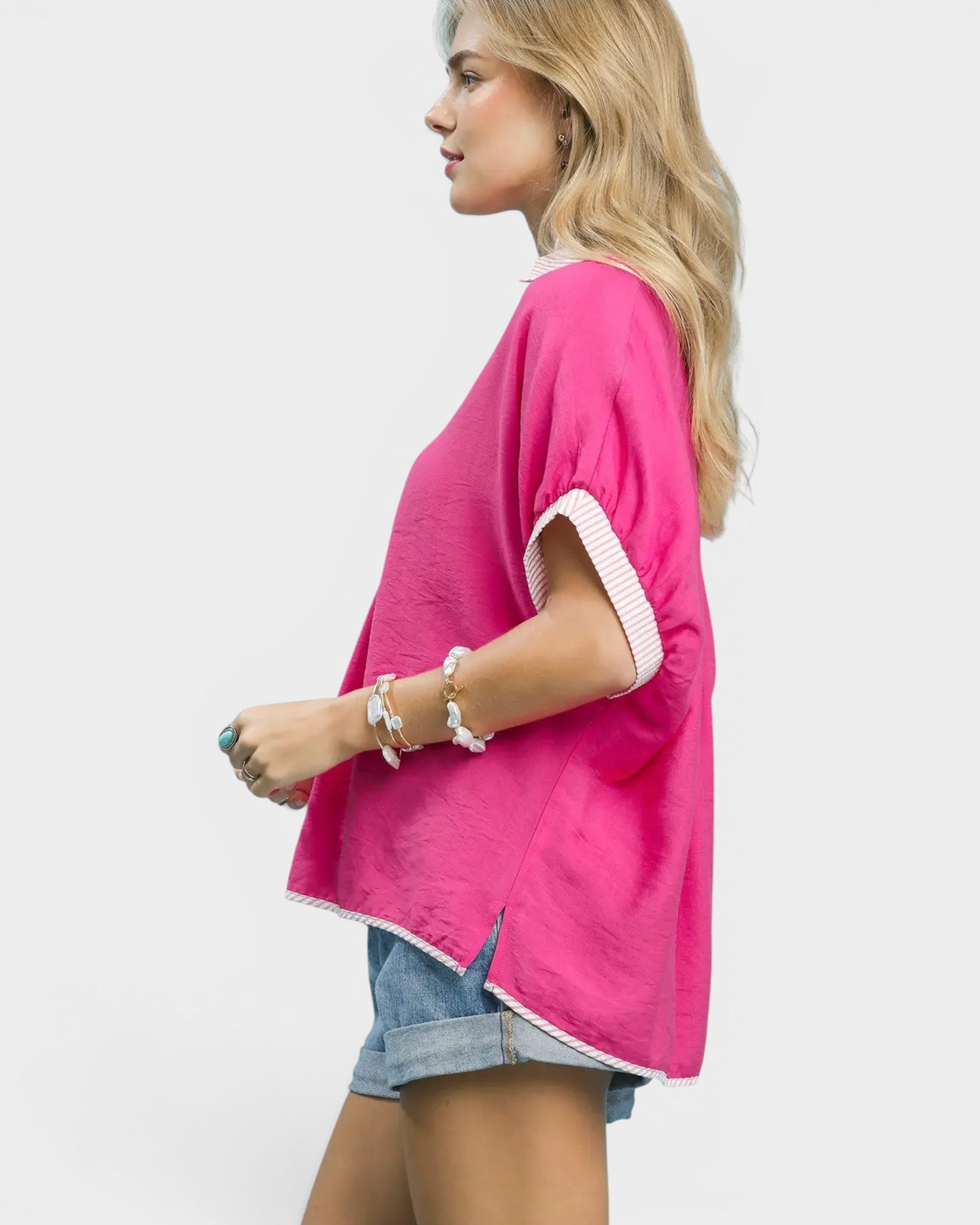 Woman wearing a bright pink top with white trim on a plain background