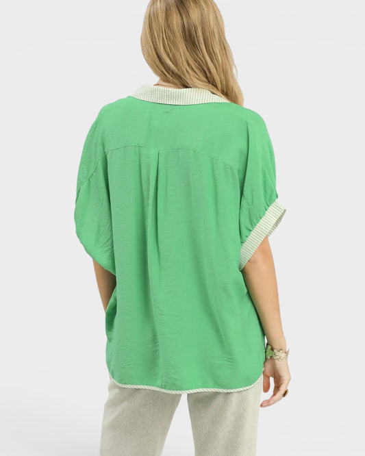 Person wearing a green blouse with white trim on a light gray background