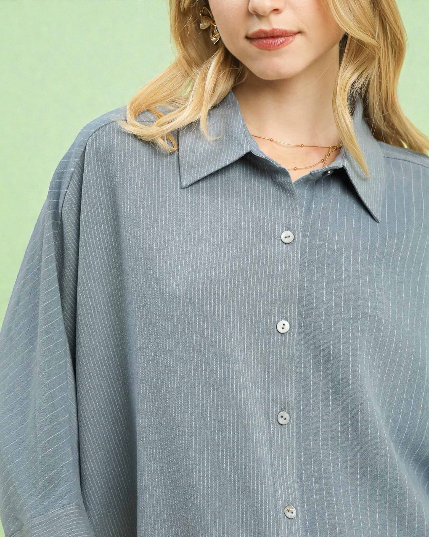 Person wearing a light blue striped shirt against a green background