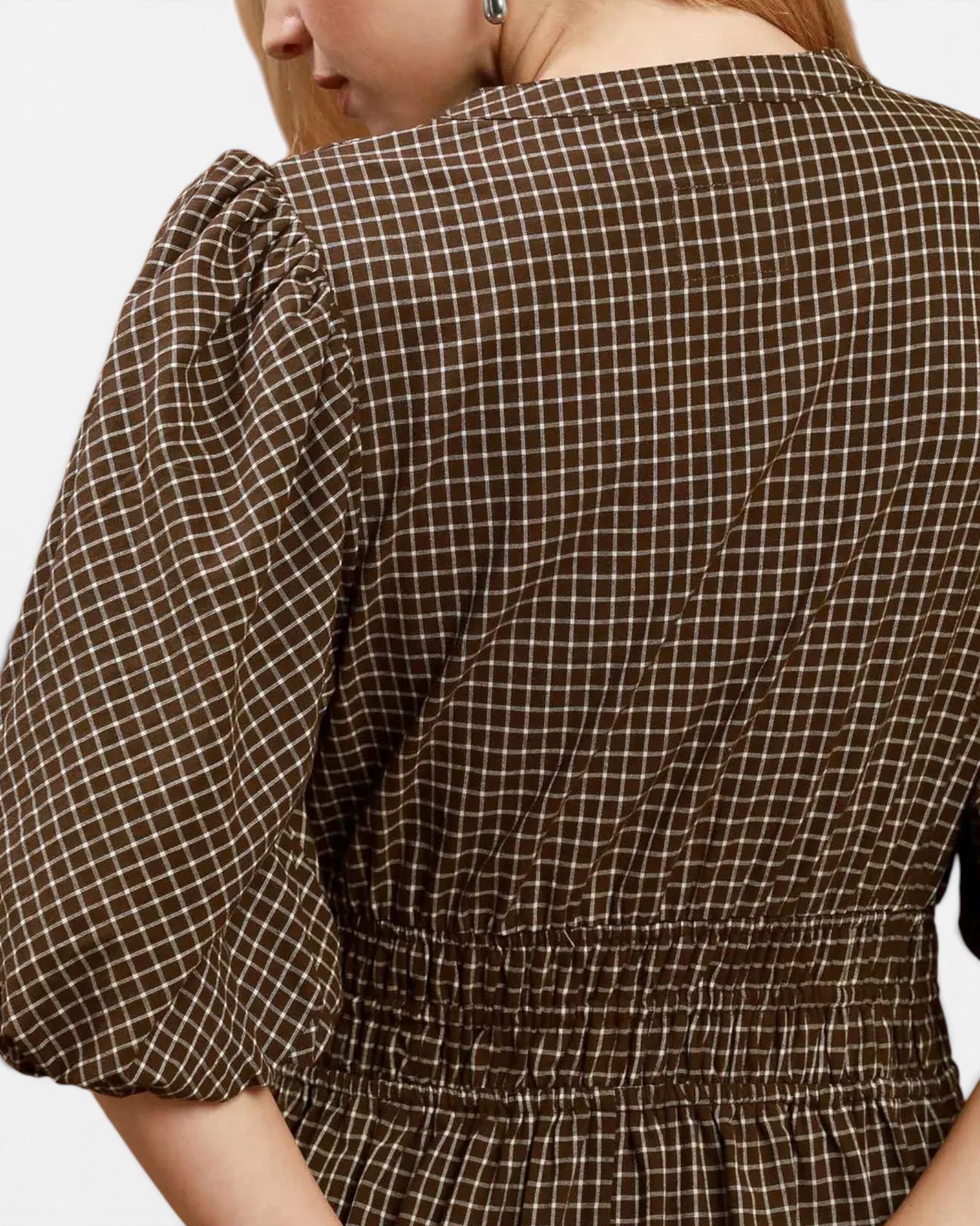 Close-up back view of a person wearing a brown and beige gingham dress with puff sleeves and a smocked waist.