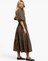 A woman modeling a brown and black checkered tiered midi dress with puff sleeves, paired with black flat shoes, against a plain white studio background.
