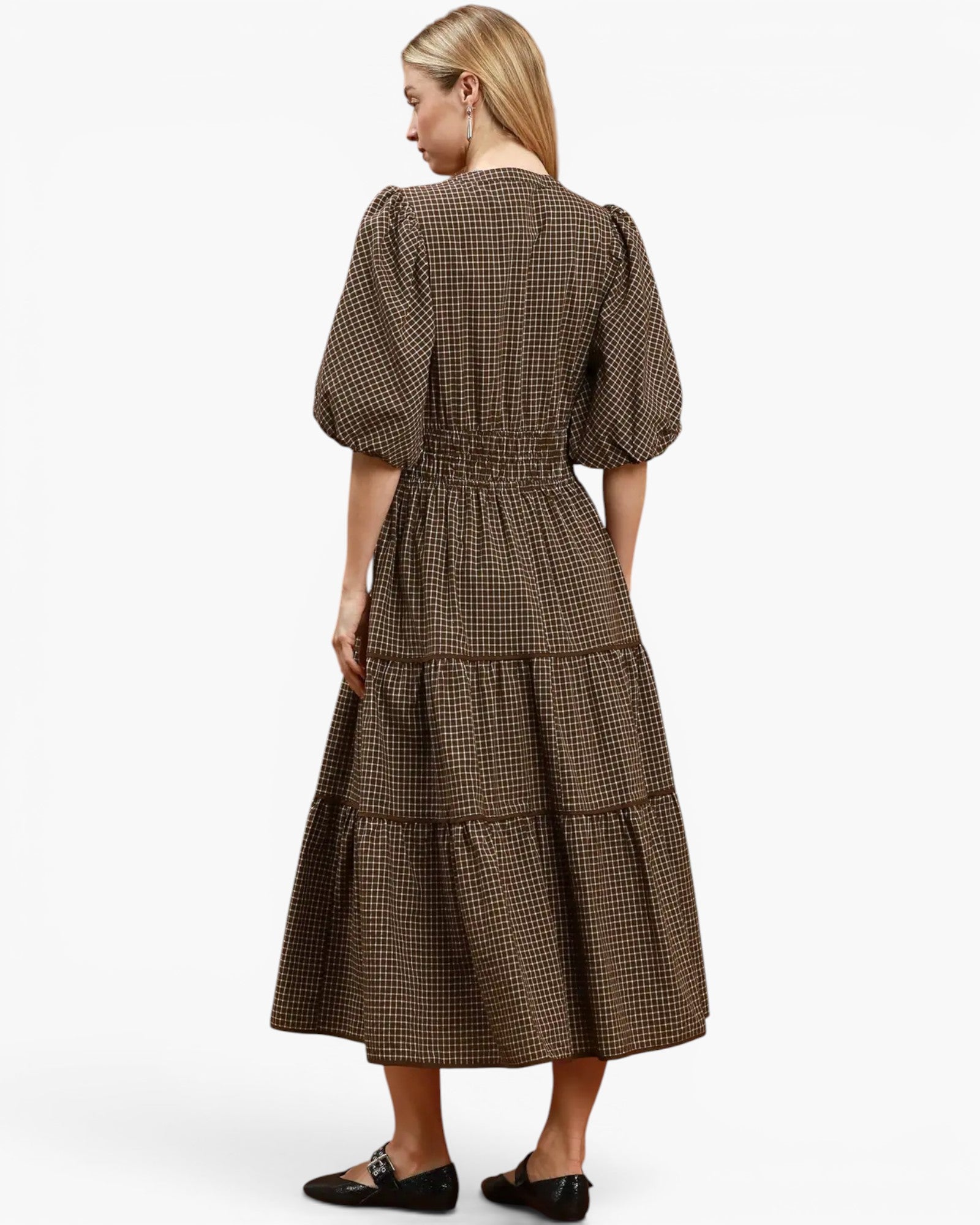 A woman shown from the back wearing a brown and black checkered midi dress with puff sleeves and a tiered skirt, paired with black flats, against a plain white studio background.