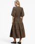 A woman shown from the back wearing a brown and black checkered midi dress with puff sleeves and a tiered skirt, paired with black flats, against a plain white studio background.