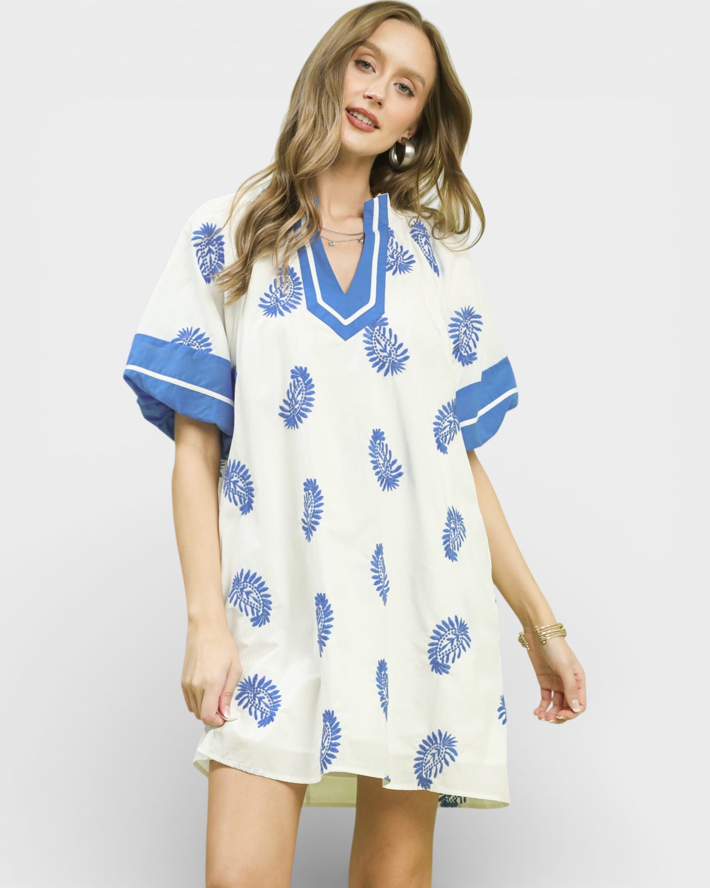 Woman wearing a white dress with blue floral patterns on a plain background