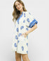 Woman wearing a white dress with blue floral patterns on a plain background