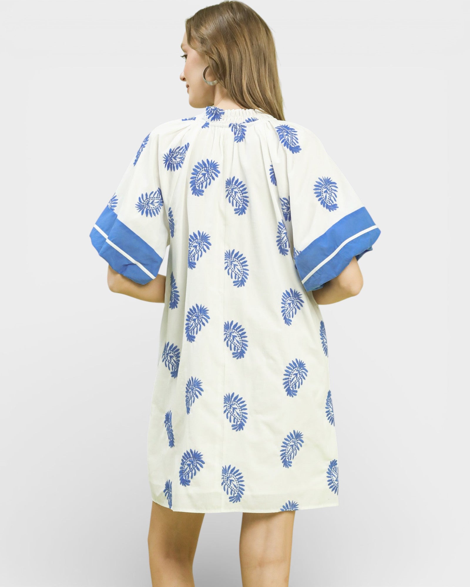 Woman wearing a white dress with blue patterns and sleeves on a light gray background