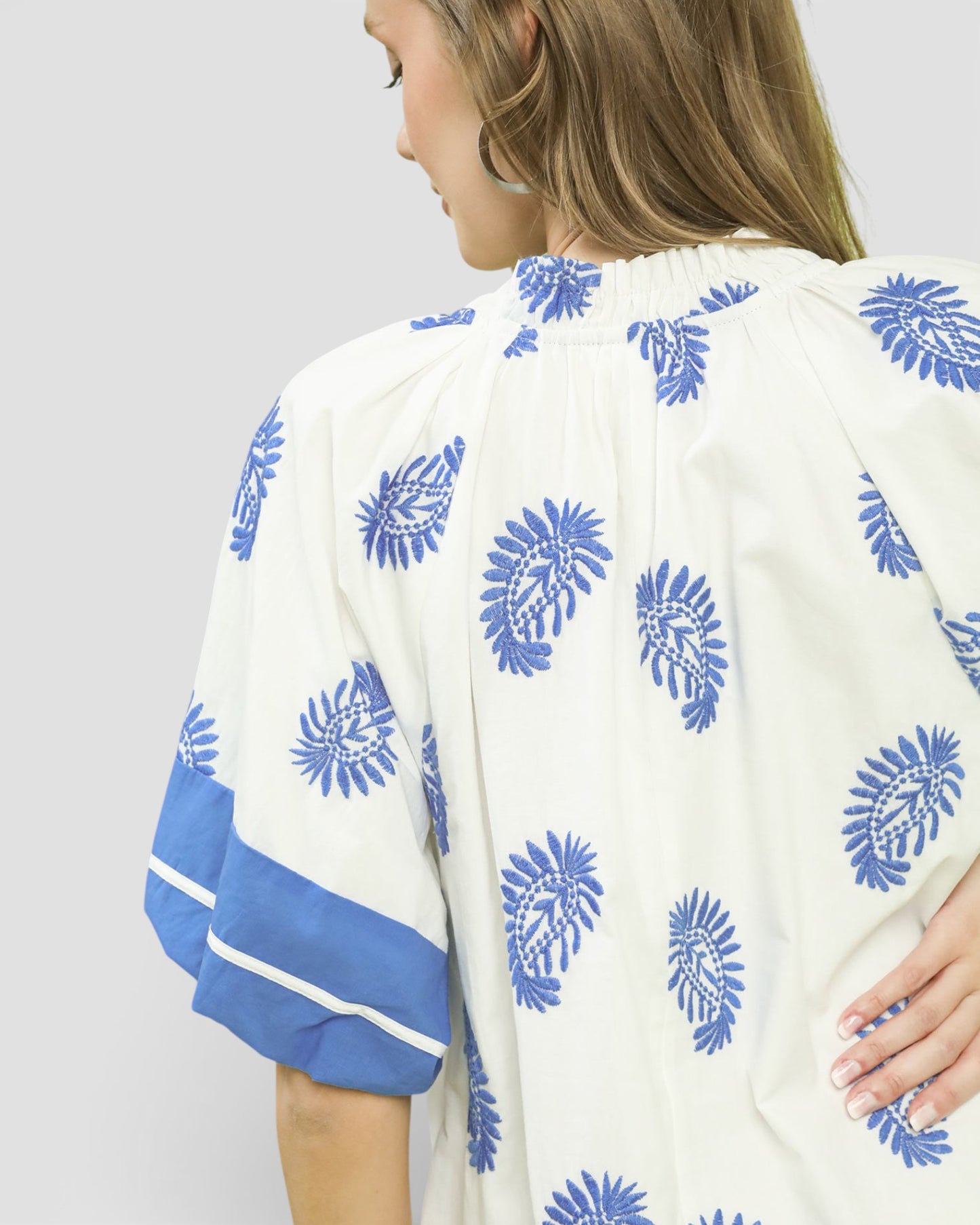 Woman wearing a white kimono-style garment with blue floral patterns on a plain background