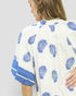 Woman wearing a white kimono-style garment with blue floral patterns on a plain background