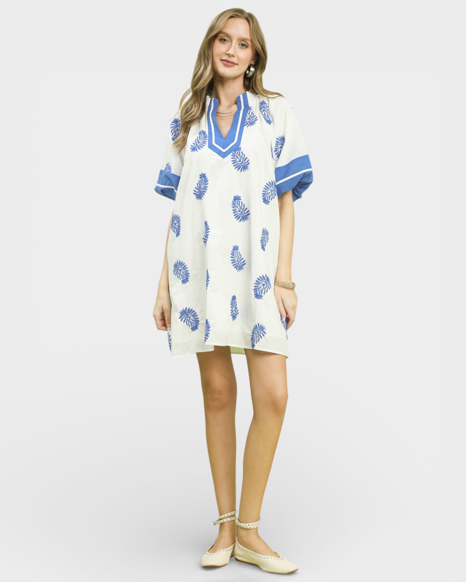 Woman wearing a white dress with blue floral patterns on a plain background