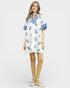 Woman wearing a white dress with blue floral patterns on a plain background