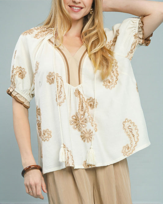 Woman wearing a white blouse with gold embroidery on a gray background