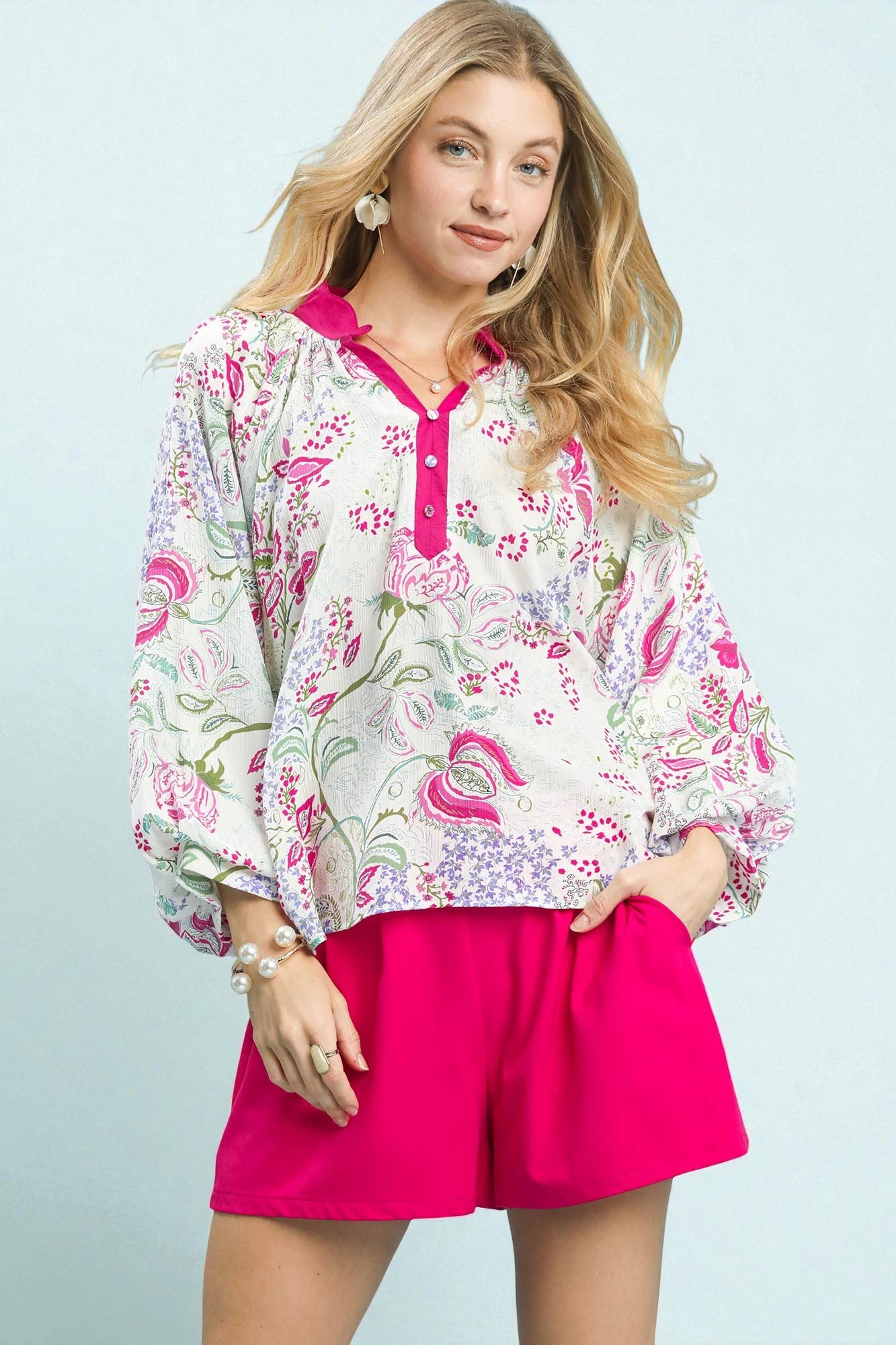 Woman wearing a floral blouse and pink shorts against a light blue background