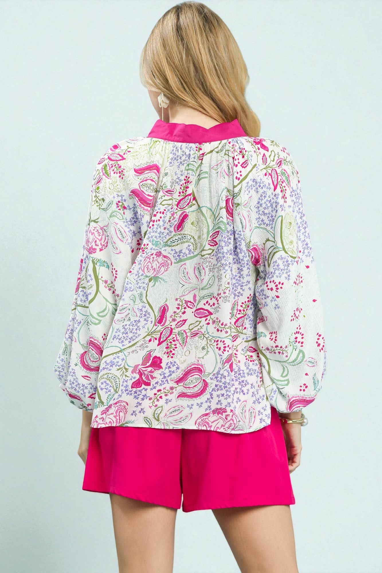 Woman wearing a colorful floral blouse and pink shorts on a light blue background