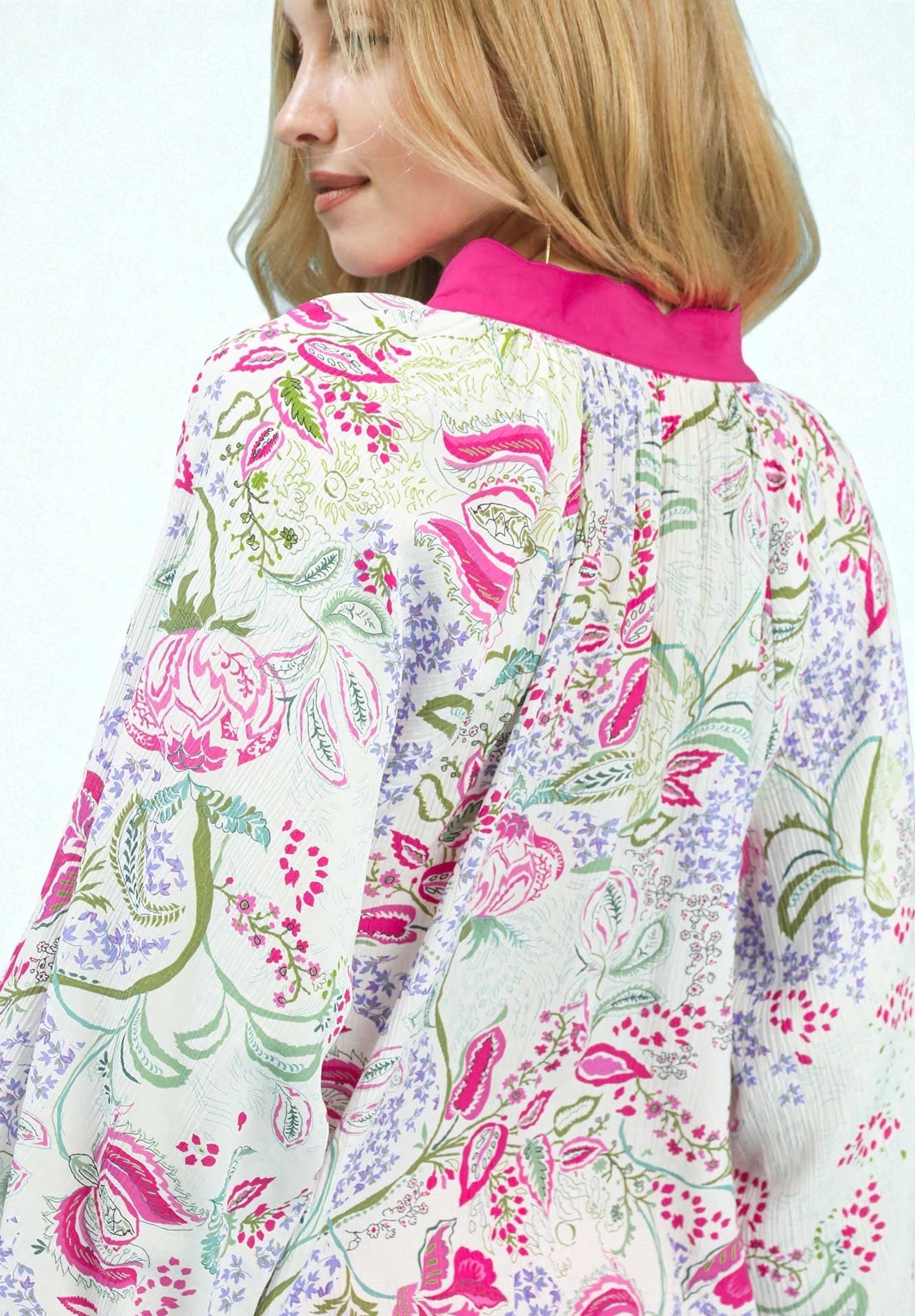 Woman wearing a colorful floral patterned shirt with a pink collar on a white background