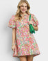 Woman wearing a colorful floral dress holding a green bag against a white background