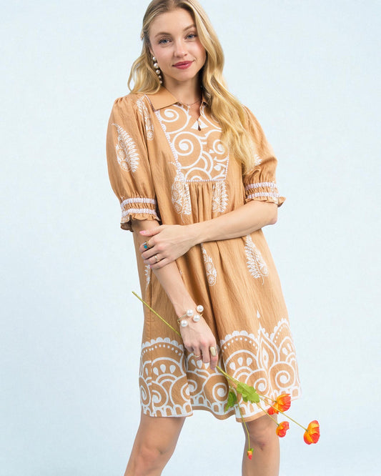 Woman wearing a tan dress with white patterns on a light blue background