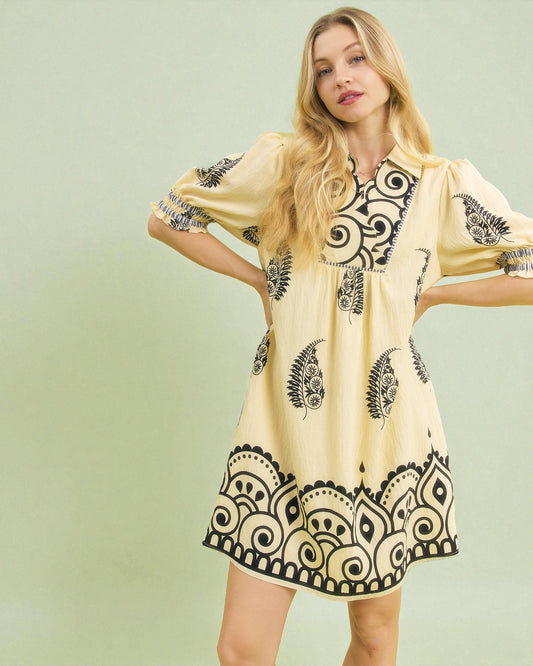 Woman wearing a yellow dress with black patterns on a light green background