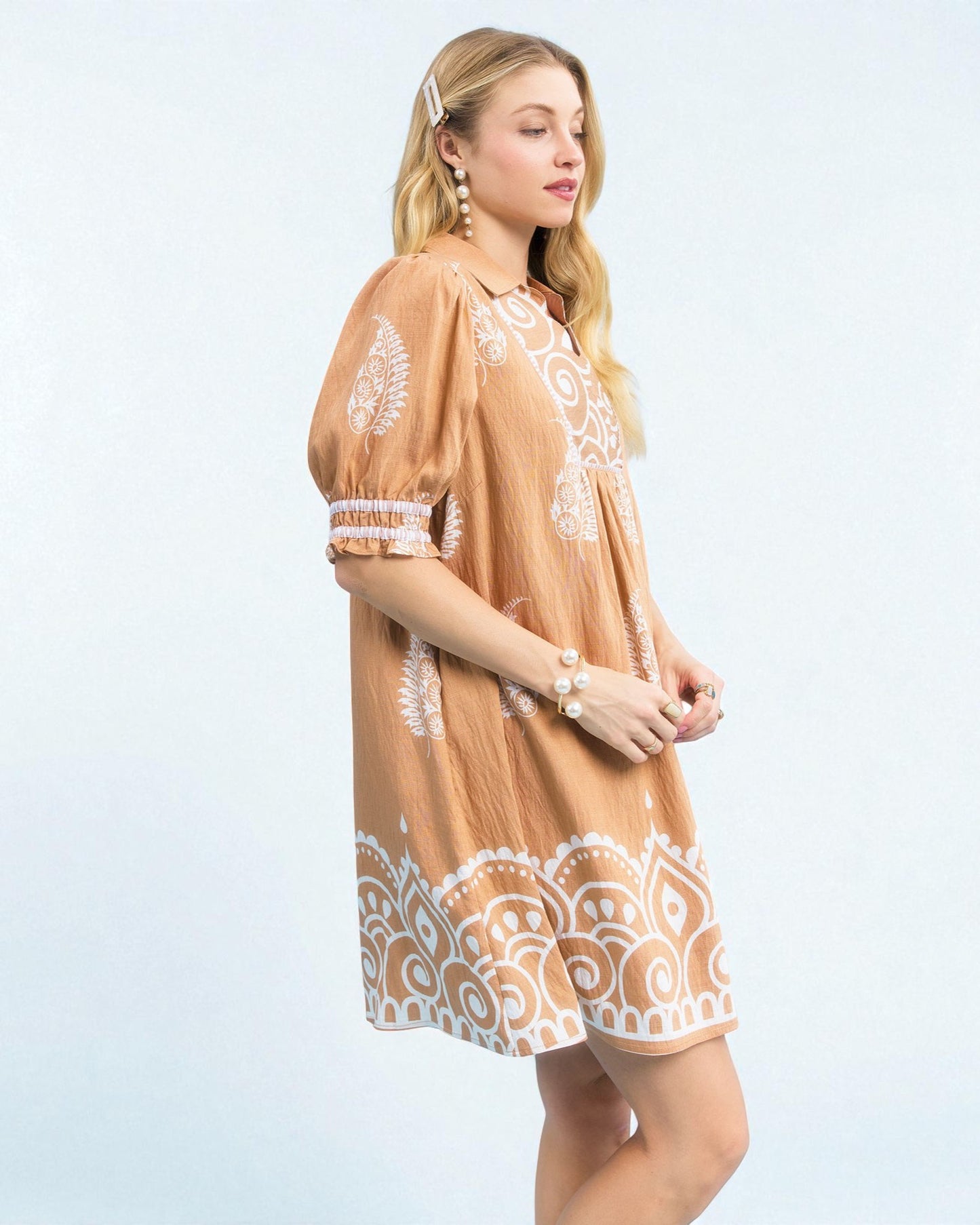 Woman wearing a tan dress with white lace details on a light blue background