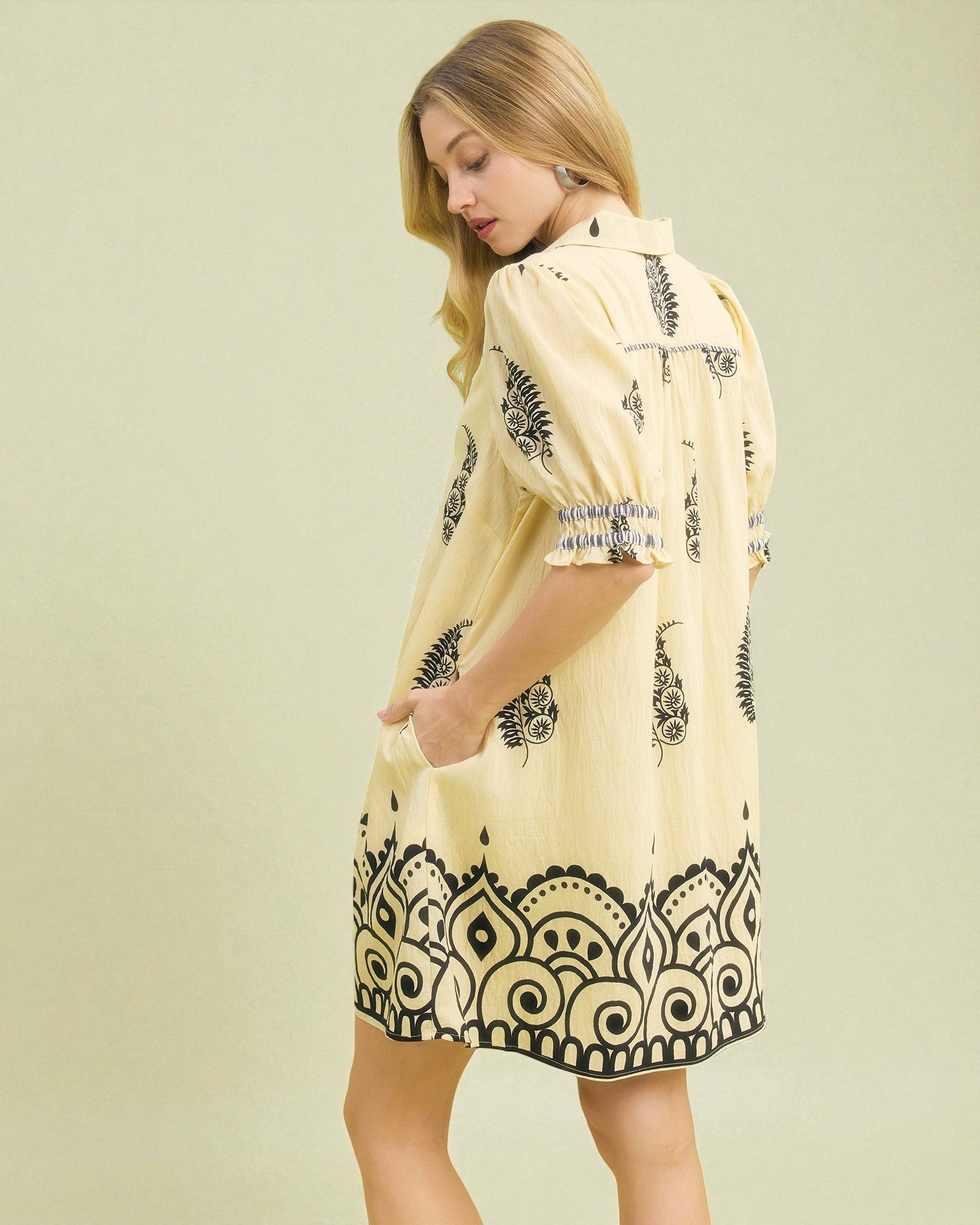 Woman wearing a yellow dress with black patterns on a light green background