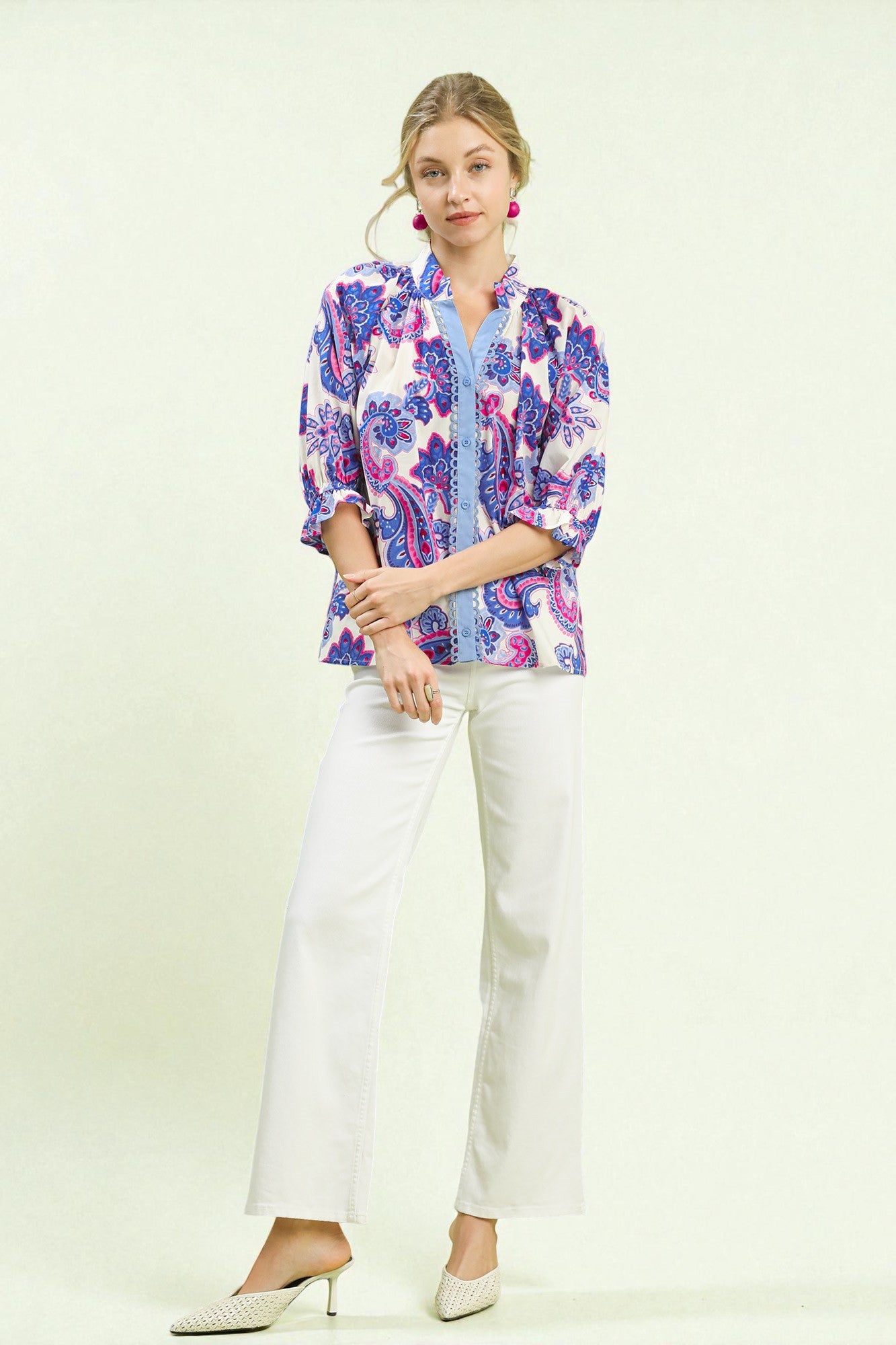Woman wearing a colorful floral blouse and white pants on a light background