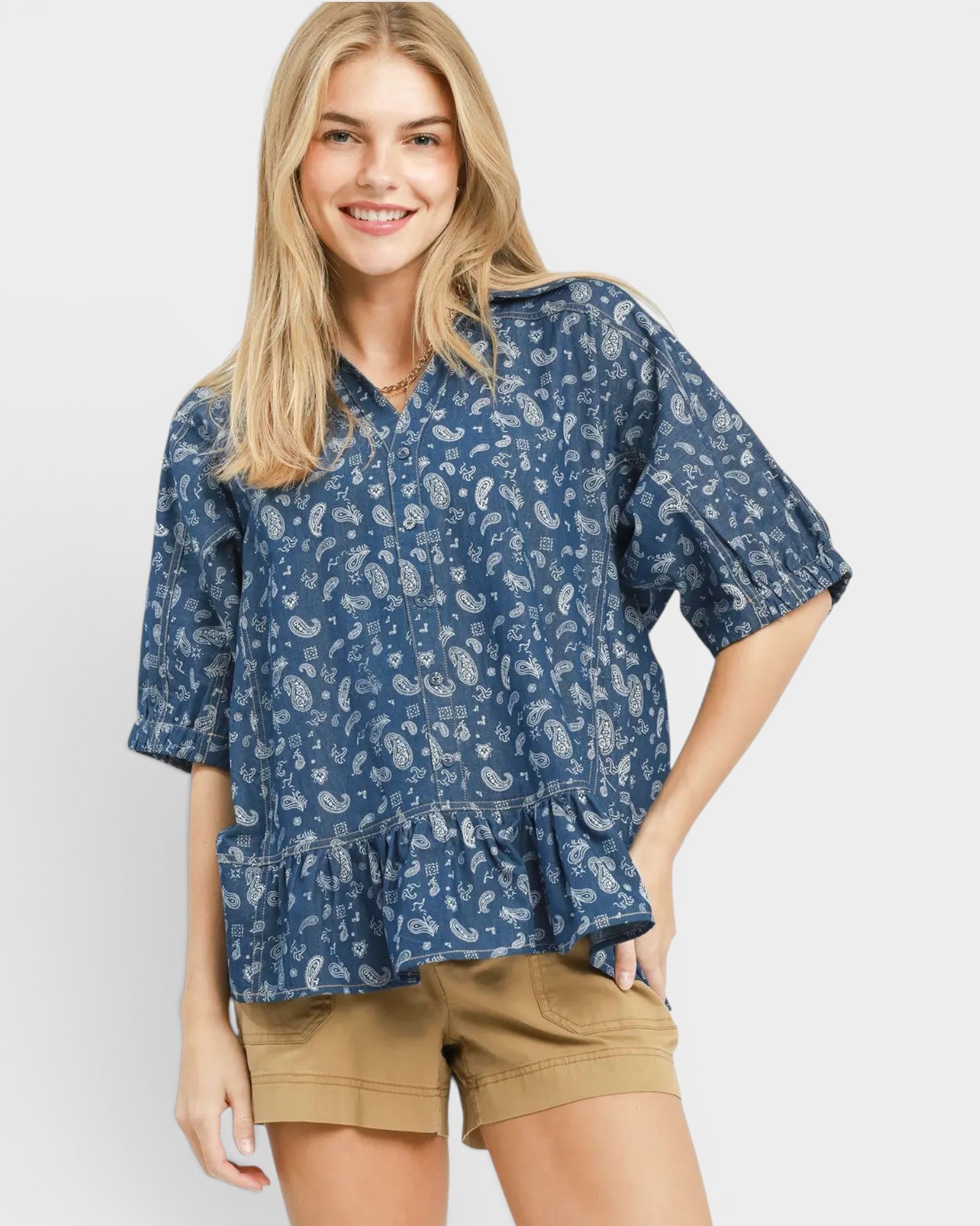 Woman wearing a blue patterned blouse and beige shorts on a white background