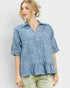 Woman wearing a blue patterned blouse with ruffled hem on a white background