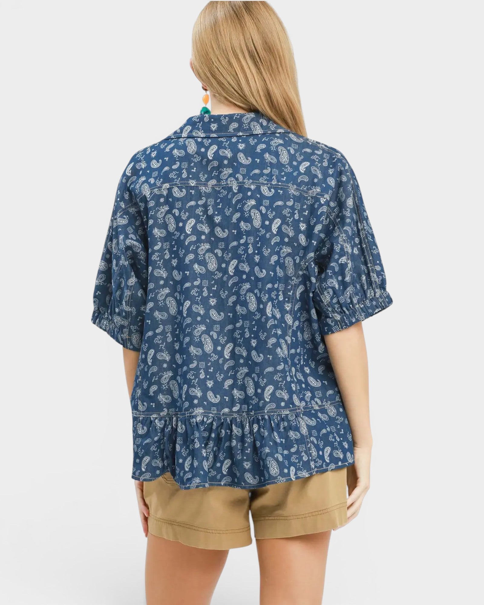 Person wearing a blue patterned shirt and beige shorts on a white background