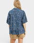 Person wearing a blue patterned shirt and beige shorts on a white background