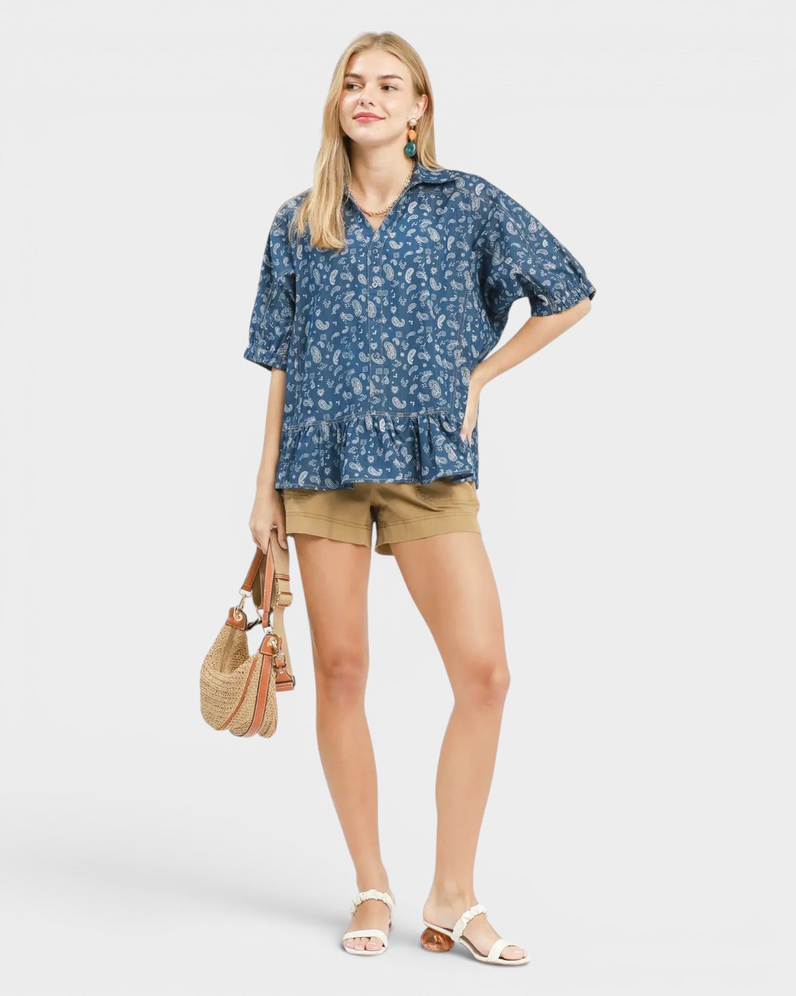Woman wearing a blue floral blouse and beige shorts on a white background