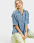 Woman wearing a blue patterned shirt and light green pants on a white background