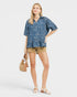Woman wearing a blue floral blouse and beige shorts on a white background