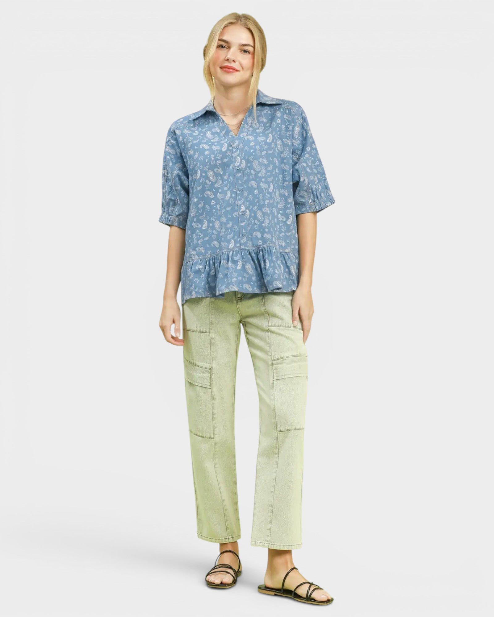 Woman wearing a blue patterned shirt and light green pants on a white background