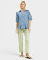 Woman wearing a blue patterned shirt and light green pants on a white background