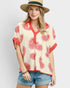 Woman wearing a patterned top with red designs, denim shorts, and a straw hat on a light gray background