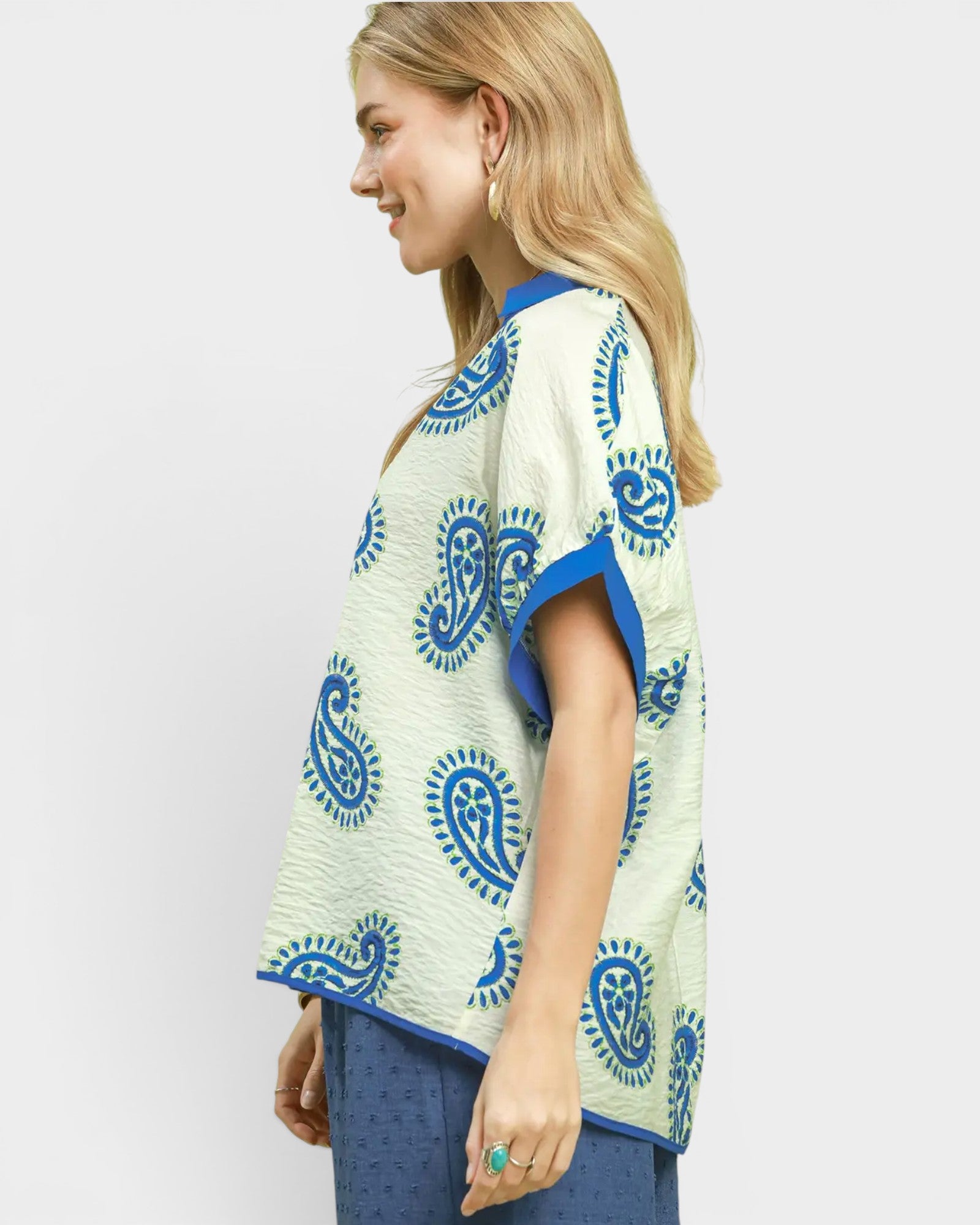 Woman wearing a white top with blue paisley patterns on a plain background