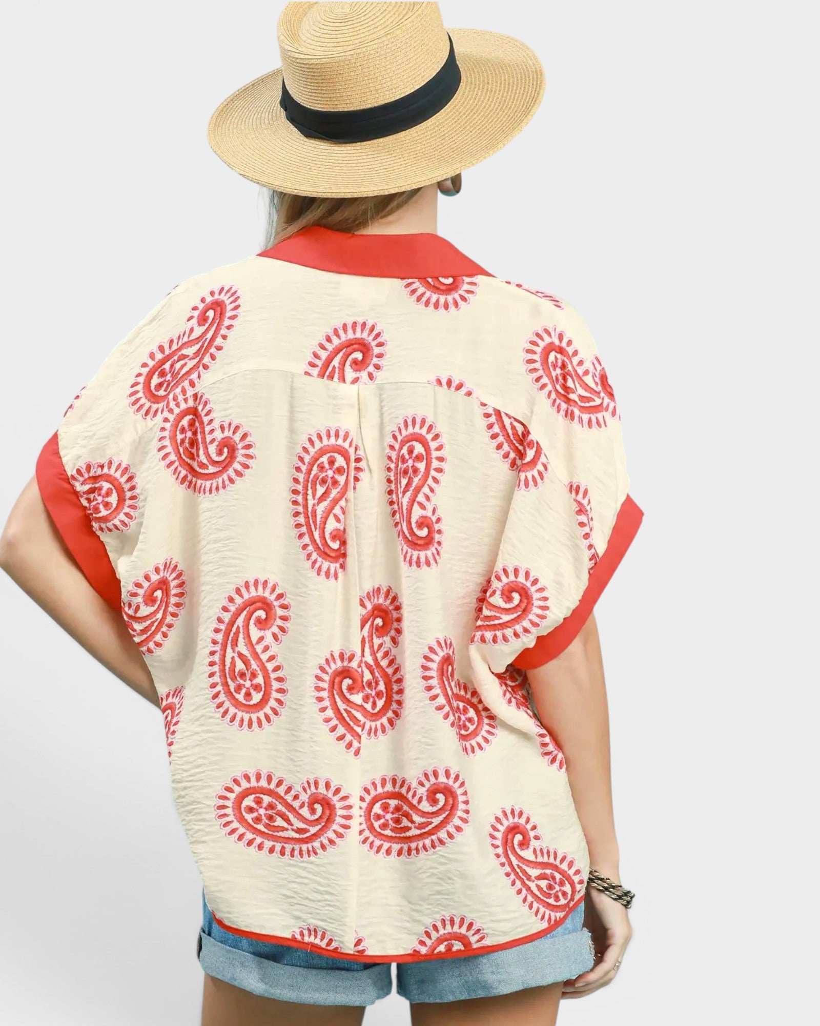 Person wearing a cream-colored top with red paisley patterns and a straw hat on a white background