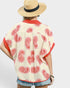 Person wearing a cream-colored top with red paisley patterns and a straw hat on a white background