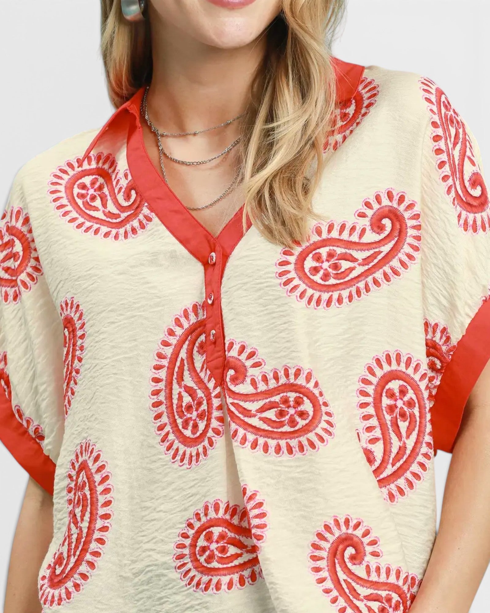 Woman wearing a cream blouse with red paisley patterns on a plain background