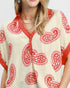 Woman wearing a cream blouse with red paisley patterns on a plain background